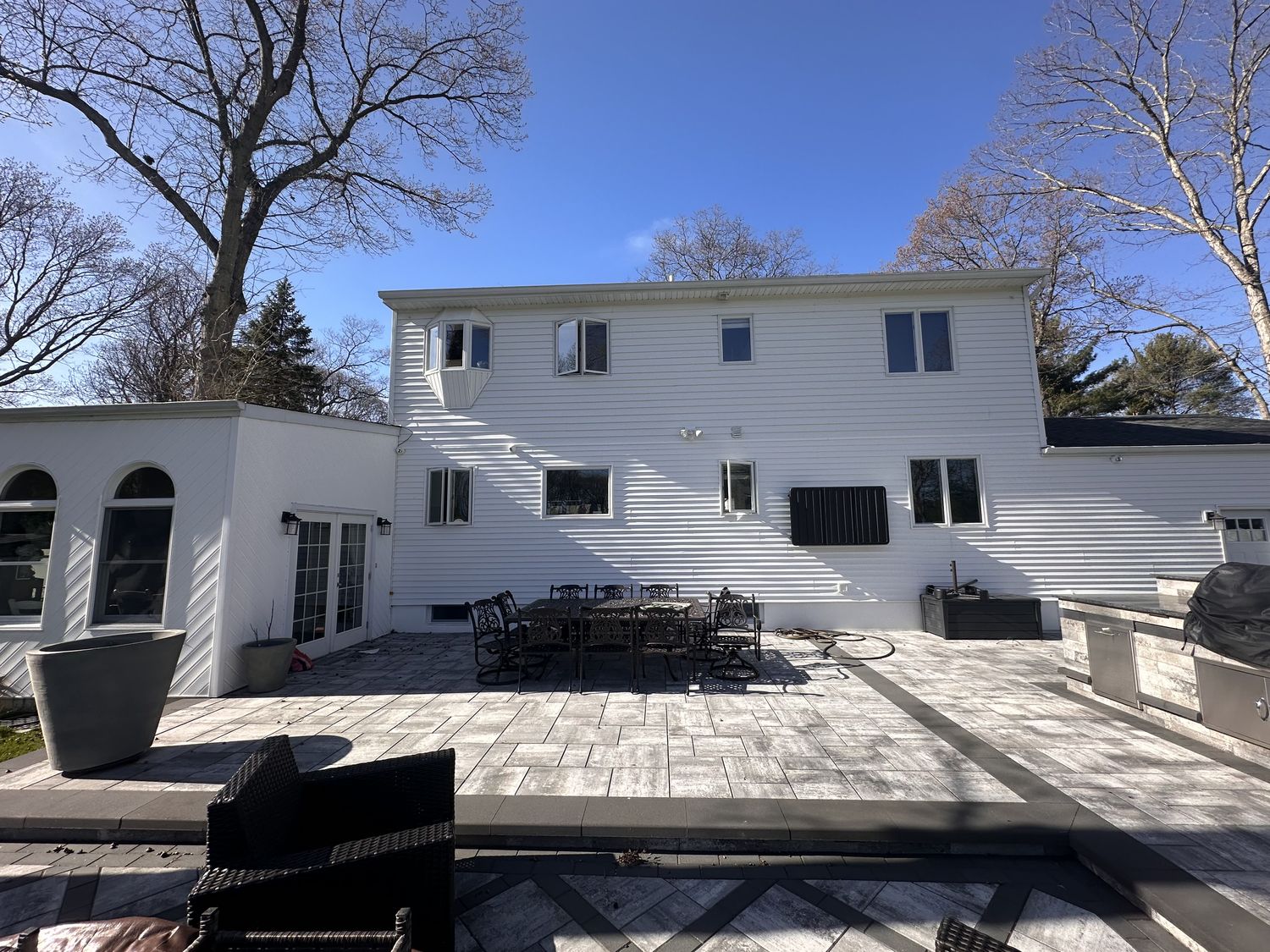 Rear of a two-story home with a large paver patio addition on Long Island